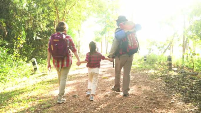 后视图: 祖父母周末与孙女一起远足，并在森林中走到阳光下