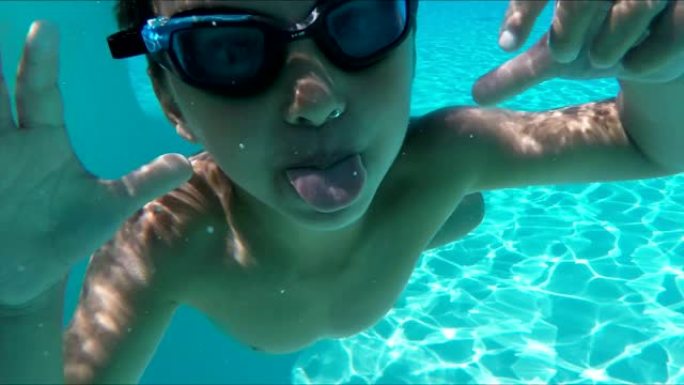 男孩在游泳池水下潜水，开始做鬼脸，露出舌头