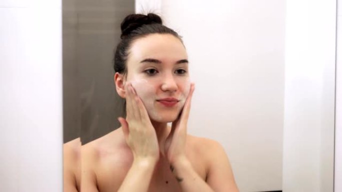 快乐迷人的年轻女子用洁面乳洗脸。