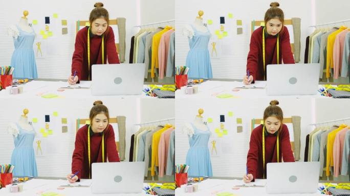 亚洲女性时装设计师在工作室工作时使用笔记本电脑，工作场所，亚洲小企业概念