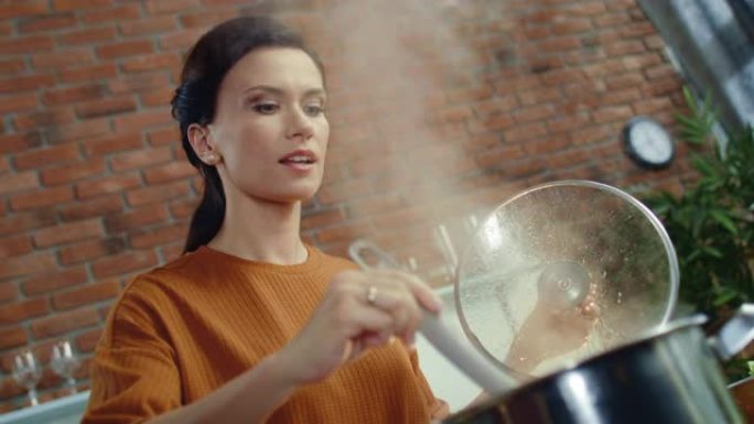 优雅的女人用勺子搅拌汤。年轻女孩从沸腾的锅里闻到食物。