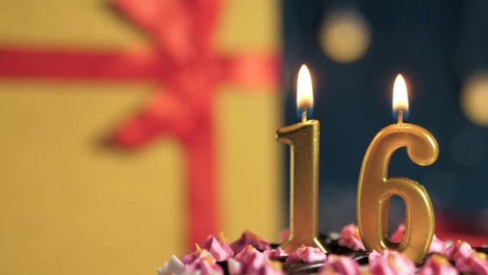 生日蛋糕编号16点灯燃烧的金色蜡烛，蓝色背景礼物黄色盒子用红丝带绑起来。特写和慢动作