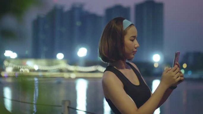 亚洲女子晚上在公园跑步后使用智能手机