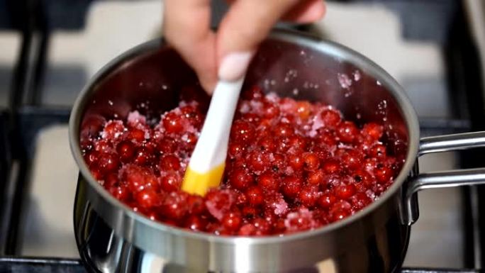 特写女人在金属平底锅中用小硅胶刮刀搅拌红莓。