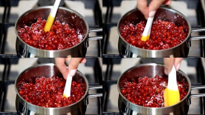 特写女人在金属平底锅中用小硅胶刮刀搅拌红莓。