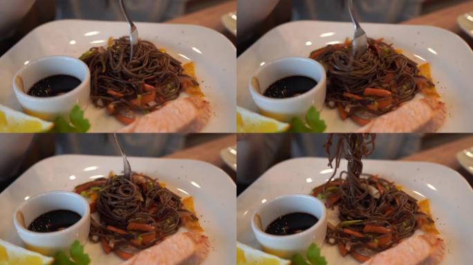 白盘荞麦面配三文鱼和酱油的美味菜肴特写。女人的手在叉子上扭面条