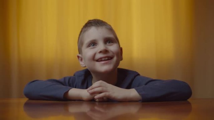自闭症男孩的肖像坐在办公桌前表现出情感。自闭症孩子在家里笑得开心。自闭症意识