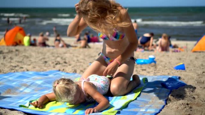 顽皮的母亲为躺在海滩垫子上的小女儿女孩做按摩