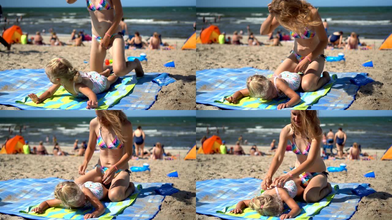 顽皮的母亲为躺在海滩垫子上的小女儿女孩做按摩