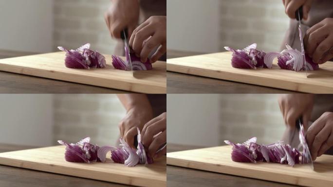 厨师手在厨房准备烹饪配料的木制切板上用刀切红洋葱的特写