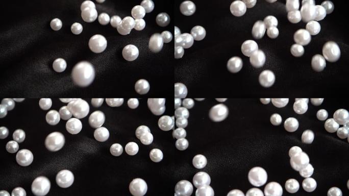 白色珍珠落在黑色织物上。慢动作。