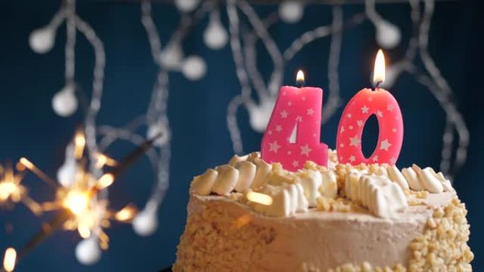 生日蛋糕，40号粉色蜡烛和蓝色背景上的烟火。慢动作和特写视图
