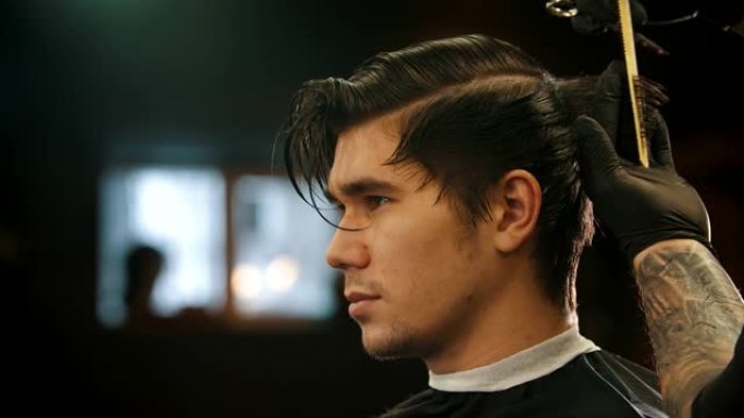 一个年轻的男人在理发店理发，纹身的理发师戴着黑色手套-剪颈背