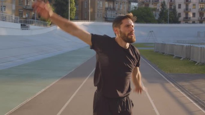 成人高加索运动型男性慢跑者的特写肖像早上在城市户外的体育场上伸展手臂