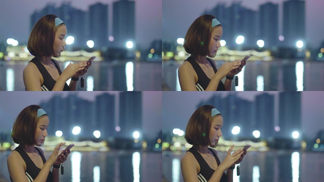 亚洲女子晚上在公园跑步后使用智能手机