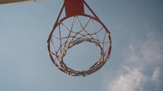 特写镜头自下而上查看篮球在球场上被扔进篮筐的肖像，天空多云