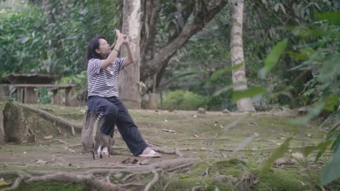 年轻女子在森林中享受大自然，并使用智能手机与可爱的猫拍照。