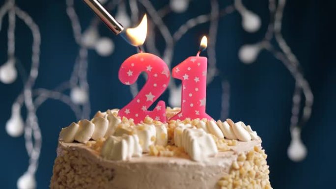 蓝色背景上有21号粉色蜡烛的生日蛋糕。蜡烛着火了。慢动作和特写视图