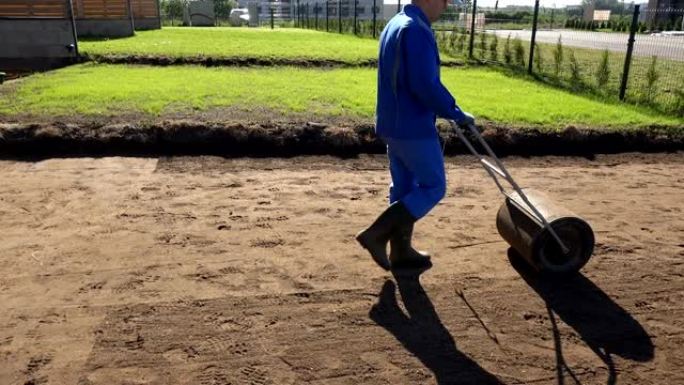 园丁人在播种草坪后使用压路机硬化土壤。手持