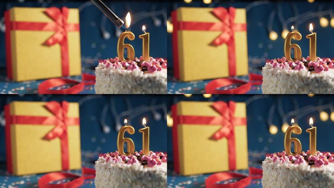白色生日蛋糕编号61点灯燃烧的金色蜡烛，带灯的蓝色背景和用红丝带绑起来的礼物黄色盒子。特写