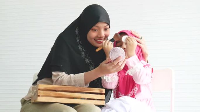 年轻的穆斯林女孩喜欢和她的小孩一起在白色背景的房间里用化妆品化妆活动