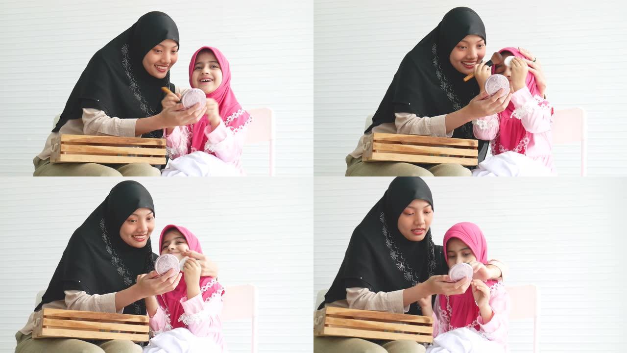 年轻的穆斯林女孩喜欢和她的小孩一起在白色背景的房间里用化妆品化妆活动