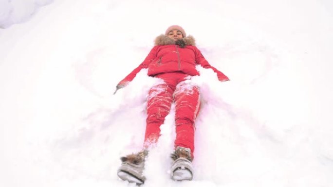 在冬季公园的雪地上穿着红色西装的女人在公园里做一个雪天使的身影。复制空间文本