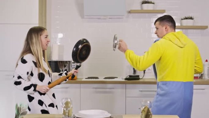 幸福的夫妻在家里用rolling面杖和平底锅在厨房打架很开心。