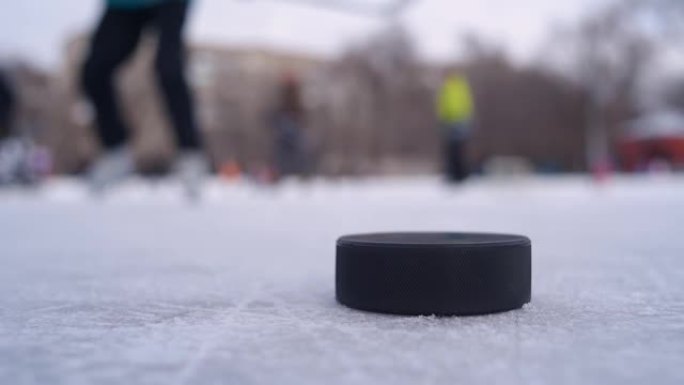 一个黑色的冰球躺在冰上，男人在背景中打曲棍球