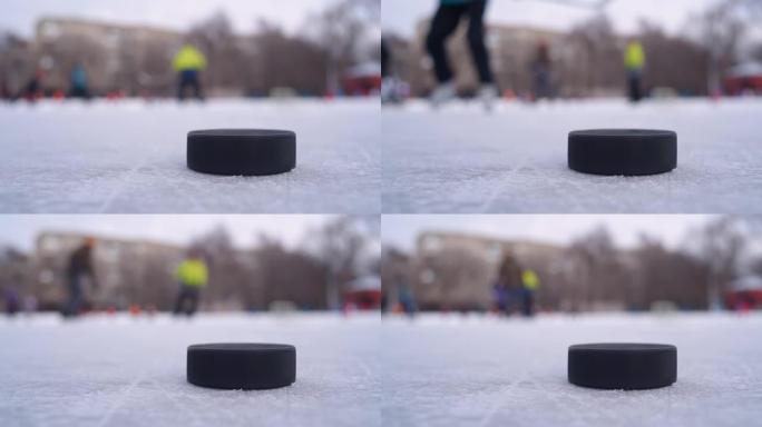 一个黑色的冰球躺在冰上，男人在背景中打曲棍球