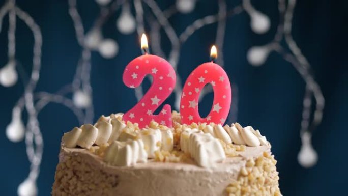 蓝色背景上有20号粉色蜡烛的生日蛋糕。蜡烛吹灭了。慢动作和特写视图
