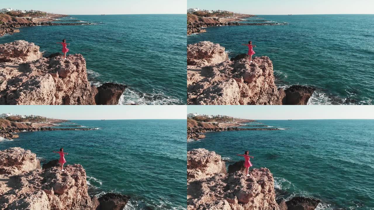 穿着红色衣服的女人站在岩石悬崖的边缘，双手伸向空中。红色连衣裙随风飘扬。在岩石悬崖上穿着红色衣服的女