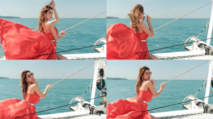 穿着比基尼的亚洲红色礼服女孩的慢动作镜头站在游艇的船头，在阳光照射下看起来放松和性感的姿势。