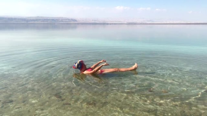 女人在死海中游泳，有趣，躺在背上，手机旅行镜头