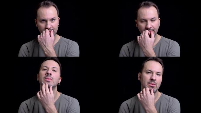 中年白人男子的肖像，耳环沉思地抚摸着他的下巴，并在黑色背景上注视着相机。