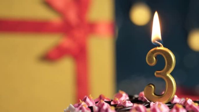 生日蛋糕3号点火器燃烧的金色蜡烛，蓝色背景礼物黄色盒子用红丝带绑起来。特写和慢动作