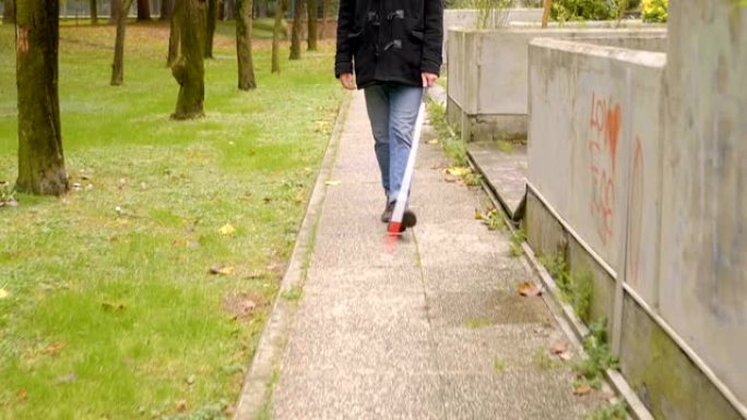 年轻英俊的盲人拄着白色拐杖在公园里散步