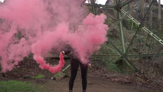 一名身穿皮夹克的年轻女子在桥下挥舞着一枚粉色烟雾弹