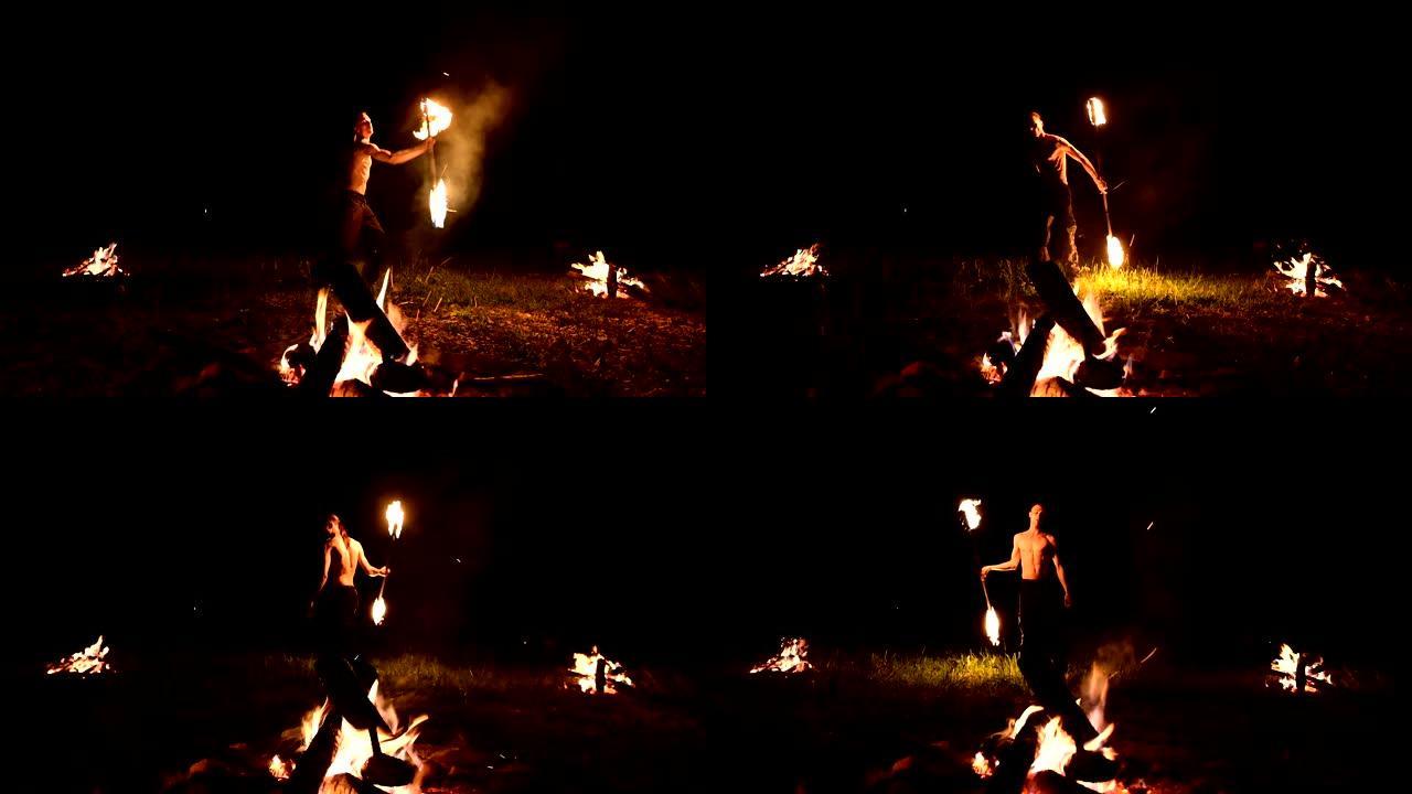 低调。一名长发，裸露躯干的年轻男性在大火附近的黑色夜晚视频慢动作中在户外旋转燃烧的火炬。现代法克尔 