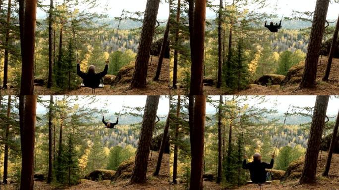 一个年轻快乐的人在森林里荡秋千，在山峡里欣赏秋天的美景。