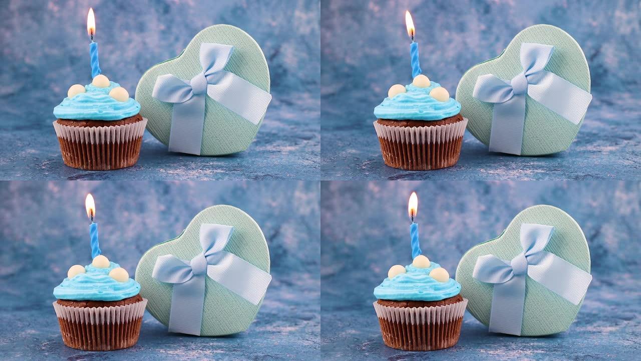 蓝色生日蜡烛在巧克力杯蛋糕上燃烧，装饰有蓝色奶油和礼物