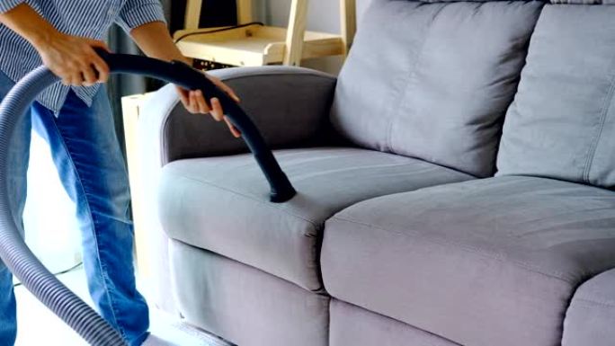 客厅带吸尘器的年轻女子清洁沙发，家务概念