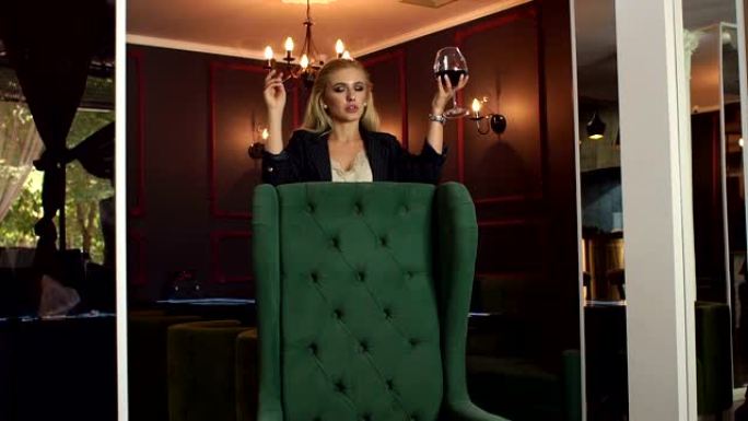一支雪茄和一杯红酒的苗条女孩正靠在绿色的椅子上。