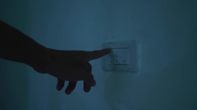 挂在墙上的灯泡在照明开关上用人的手打开。