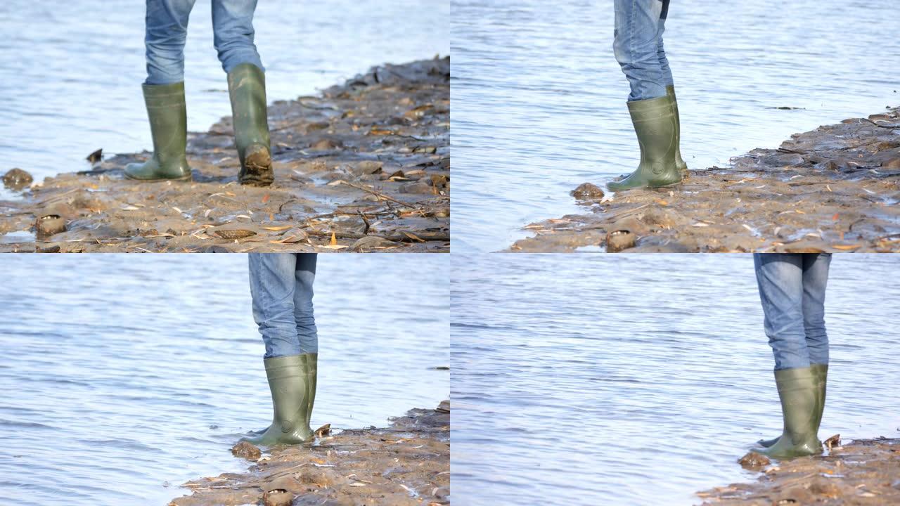一名穿着绿色橡胶靴的男子渔民正沿着水库的沼泽海岸行走