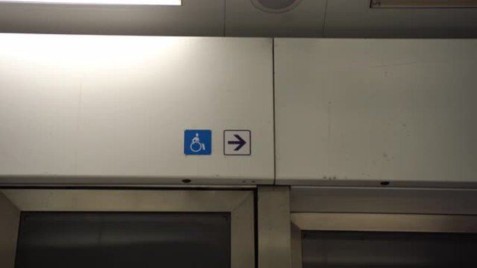 公共交通车门上方的残疾人标志，带有指向入口或出口的箭头。坐在轮椅上的人的蓝色象形文字是障碍符号。残疾