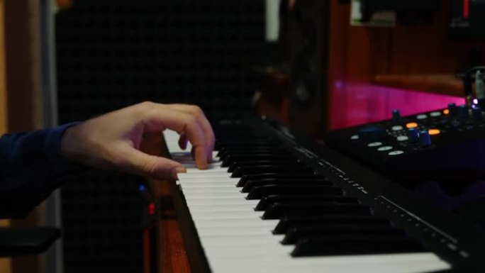 男性手在家庭音乐工作室演奏钢琴midi键盘。声音制作人在录音室创作流行摇滚歌曲。近距离弹奏电子琴。女
