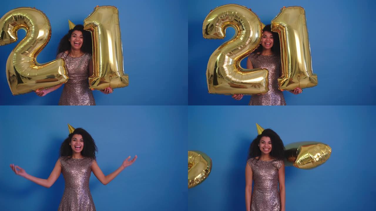 美丽的年轻非洲卷毛女人在蓝色背景上放下21号金箔庆祝气球