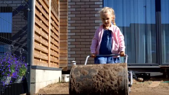 母亲帮手女孩女儿在后院用巨大的滚筒平整土壤
