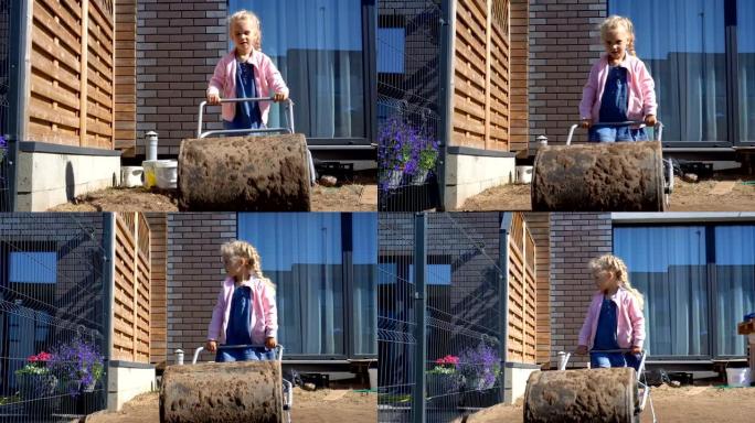 母亲帮手女孩女儿在后院用巨大的滚筒平整土壤